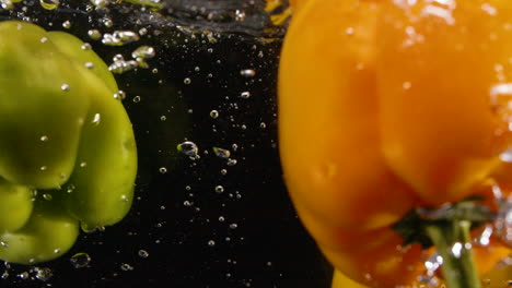Variedad-De-Alimentos-Pimientos-Salpicados-En-Agua-Limpia-Con-Burbujas-En-Cámara-Lenta-Naranja-Rojo-Verde