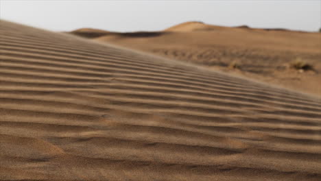 Slow-motion-sand-blowing-across-desert-in-middle-eastern-desert-landscape,-sand-dunes-in-United-Arab-Emirates-near-Dubai