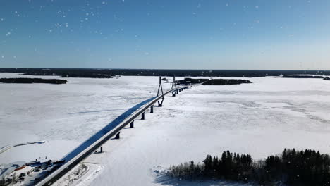 AERIAL,-Snow-falling-on-Replot-bridge-and-winter-landscape-in-Ostrobothnia-Finland