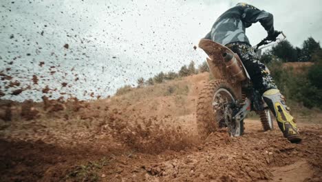 Close-up-of-a-wheel-of-a-dirt-bike-spinning-and-slinging-mud-all-over-the-place,-offroad-concept