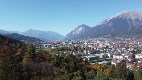 Vista-Aérea-De-La-Ciudad-De-Innsbruck-Desde-Las-Colinas-De-Un-Bosque-En-Un-Soleado-Día-De-Otoño-Y-Un-Cielo-Azul-Y-En-El-Fondo-Los-Alpes,-Tirol,-Austria,-Europa