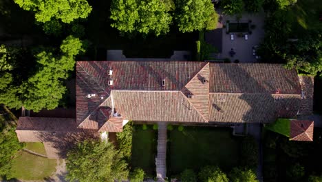 Drone-Top-Shot-of-a-Southern-French-Castle's-Rooftop-with-Twin-Towers,-Surrounded-by-Trees-and-Gardens