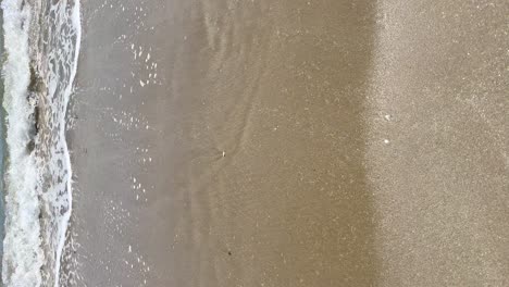 foam-with-waves-of-the-sea-on-the-beach-from-a-vertical-shot-view,-vertical-view
