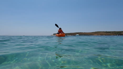 Water-level-view-of-a-woman-with-an-orange-kayak-passing-by-at-sea