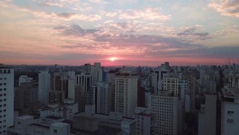 Descending-aerial-shot-of-sunset-in-Sao-Paolo-city-center,-pink-red-color-sky-and-sun