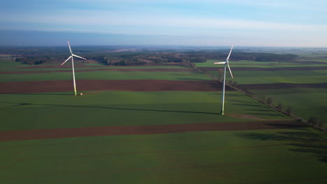 Aerial-view-of-two-wind-turbines-producing-green-energy-on-farm-field-during-cloudy-day---panorama-wide-shot
