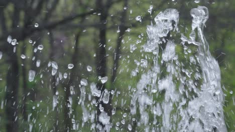 Splashing-bubbling-clear-fountain-water-against-park-tree-greenery-outside