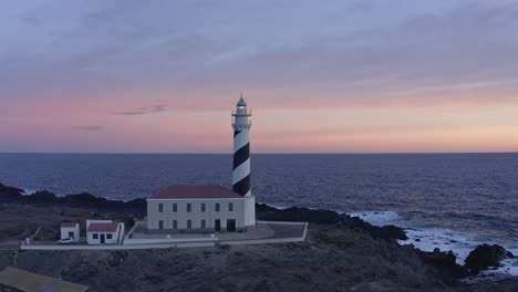 Sunset-at-Favaritx-lighthouse-in-Menorca,-Spain-with-drone-flight-around-the-structure