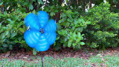 Blue-pinwheel-spinning-as-wind-blows,-bushes-in-background