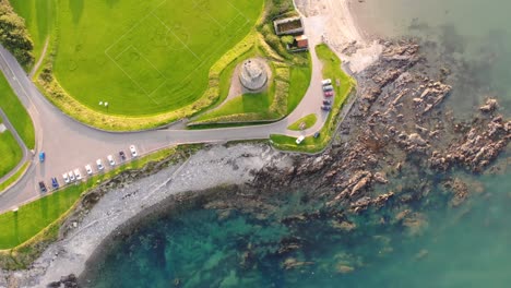 Footbal-pitch,-old-tower,-and-underwater-rock-formation,-Ireland-seaside,-aerial-drone-shot-birds-eye-view