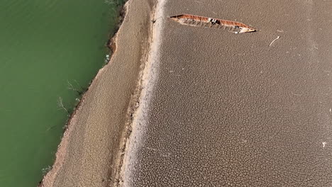 Shipwreck-on-cracked-land-of-lake-during-extreme-drought,-aerial-drone-view