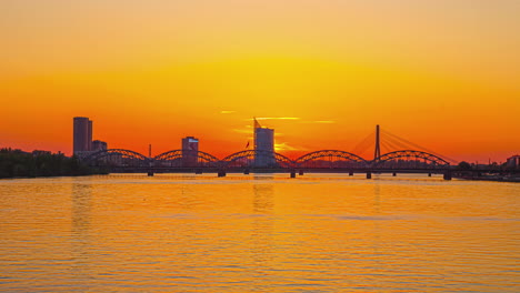 Sonnenuntergang-über-Einem-Fluss-Mit-Der-Silhouette-Von-Brücken-Und-Der-Skyline-Der-Stadt-Im-Hintergrund---Zeitraffer