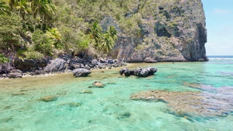 Slow-forward-flight-over-crystal-clear-water-with-rocks-and-coral-reef-at-Playa-Fronton-in-front-if-steep-mountain---Las-galeras,-Samana
