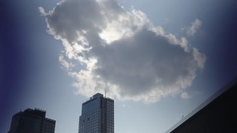 A-wandering-cloud-momentarily-obscures-the-sun-over-a-towering-high-rise-building-in-Brooklyn,-under-an-otherwise-clear,-serene-blue-sky