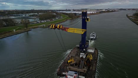 Cargo-crane-transport-ship-navigating-through-the-canal-on-a-cloudy-day-in-Zwijndrecht,-The-Netherlands