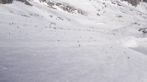 Wide-overview-drone-shot-of-people-skiing-down-a-snowy-ski-slope-on-the-Kitzsteinhorn-mountain-in-Austria-on-a-sunny-day