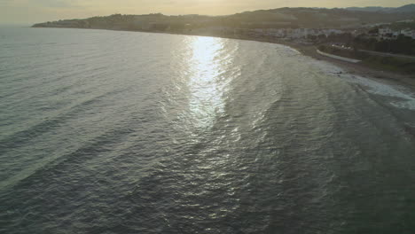 Drone-flying-backwards-over-the-bay-of-Mijas-Costa,-Spain,-during-sunset-with-overcast-sky