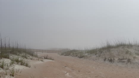 Foggy-beach,-ocean-walkway-and-sand-dunes-on-misty-morning