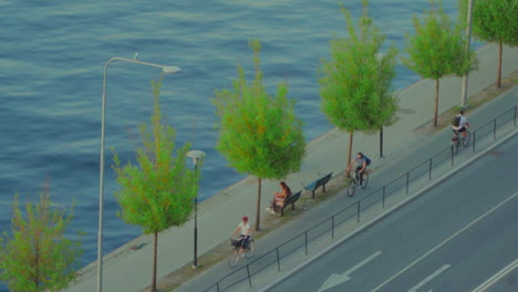 Aerial-shot-of-a-woman-sitting-on-a-bench-by-the-coast-of-Stockholm-with-people-bicycling