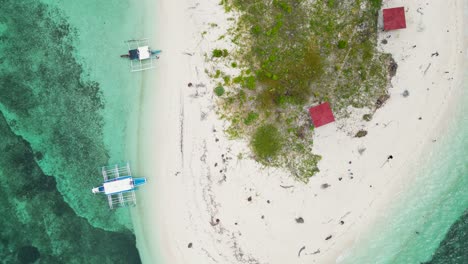 Banca-outrigger-boats-on-shore-of-balabac-island-by-beach-bungalow-huts,-aerial