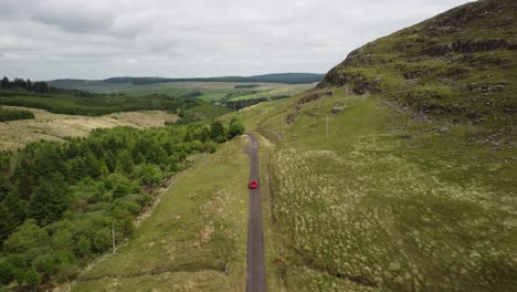 Red-vehicle-tracked-from-high-driving-along-single-track-countryside-road