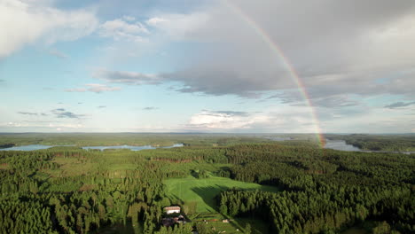 Stunning-Rainbow-over-Beautiful-Serene-Forest-and-Lake-Landscape-in-Finland,-Farm-Houses-in-the-Foreground,-Near-Kuopio,-Camera-Pushing-in