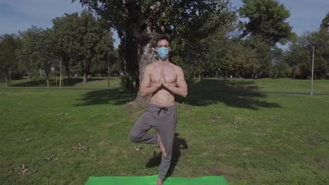 Slow-cinematic-shot-of-young-caucasian-muscular-man-doing-complex-youga-tree-pose-in-the-park