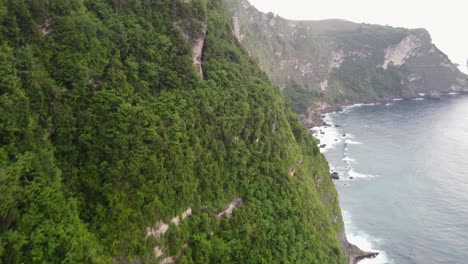 Aerial-Ascending-to-Tropical-treehouse-Airbnb-Hotel-up-on-high-steep-coastal-cape-edge-overlooking-the-waves-of-indian-ocean-crashing-down-the-green-vegetated-cliff
