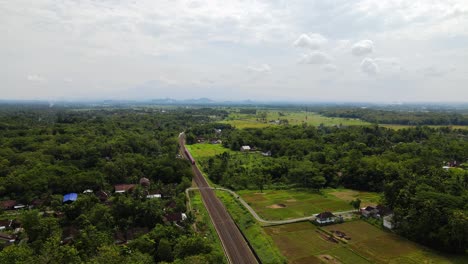 Aerial-drone-view-following-a-train-running-on-rails-in-a-rural-area,-Indonesia