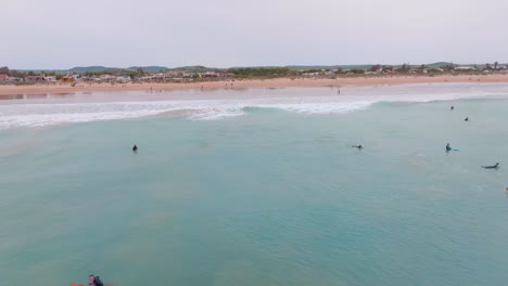 Aerial-dolly-to-beach-from-open-ocean-water-as-surfers-catch-waves-in-Spain