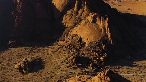 Aerial-view-overlooking-red-sandstone-cliff-in-the-Namib-desert,-sunset-in-Namibia