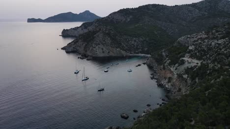 Drone-view-of-cliffs-and-looks-Sailboats-Docked-in-Cala-D'egos-Beach,-Spain