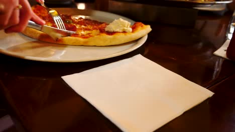 A-female-cutting-a-pizza-with-a-fork-and-knife-in-a-pub