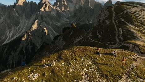 Drone-shot-over-people-on-a-mountain-ridge-revealing-the-Towers-of-Mordor,-sunny-evening-in-Dolomites,-Italy