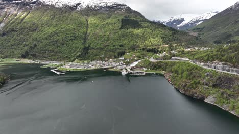 Panoramic-view-of-Hellesylt-close-to-Geiranger-Fjord-in-Norway---Spring-aerial-with-lush-green-landscape-and-snow-capped-mountains