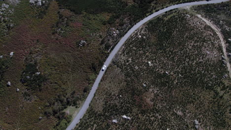 Coche-Blanco-Conduciendo-Por-Una-Carretera-Solitaria-Rodeada-De-Montañas-Y-Arbustos