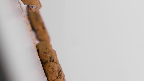 Slow-motion-vertical-shot-of-falling-vegan-cookies-with-chocolate-against-a-white-background