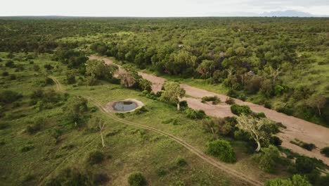 Drone-shot-tilting-up-from-a-dry-river-bed-and-a-dam-to-show-the-beautiful-african-game-park-landscape-with-mountains-in-the-background