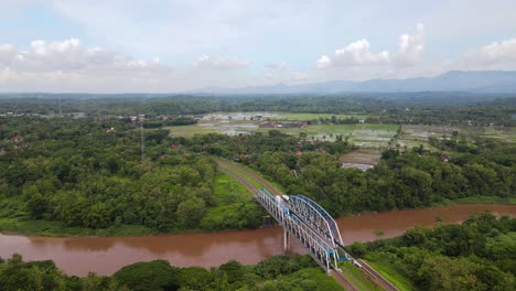 Aerial-view-of-railway-bridge-on-the-large-river-on-the-middle-of-forest-and-agricultural-land-in-Indonesian-countryside---Drone-footage