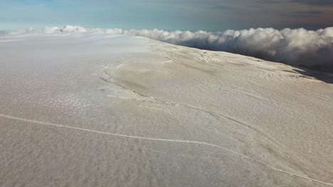 Aerial-panoramic-landscape-view-of-a-crack-on-the-ice-surface-of-an-icelandic-glacier,-over-the-clouds,-on-a-bright-sunny-day