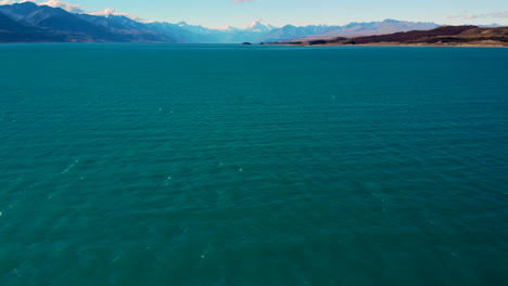 Antena-Sobre-El-Lago-Pukaki-Incline-Hasta-Aoraki,-Mt-Cook-On-Horizon,-Nueva-Zelanda