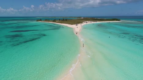 Drone-shot-people-walking-sandbank,-turquoise-sea-water-splash-on-white-sand-foam