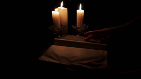 Heilige-Bibel,-Die-Bei-Kerzenlicht-An-Einem-Versteckten,-Dunklen-Ort-Gelesen-Wird-Und-Eine-Seite-Umblättert
