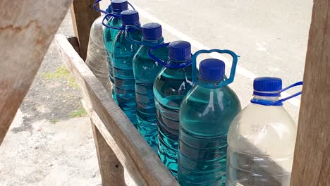 Plastic-water-bottles-filled-with-bright-blue-gasoline-petrol-fuel-at-rural-countryside-kiosk-in-Timor-Leste,-Southeast-Asia