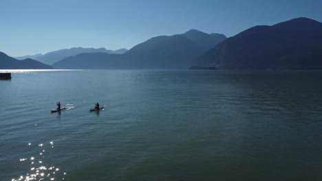 two-kayakers-paddling-back-to-shore-in-the-ocean-of-Porto-Cove,-BC