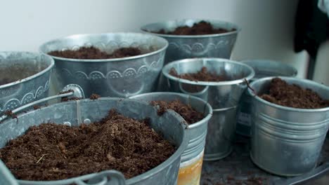 Soil-is-being-scattered-across-the-pots,-distributed-evenly-as-it-is-sprinkled-onto-each-one