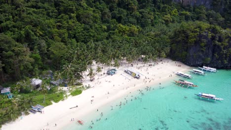 Aerial-view-:Tropical-Seven-Commandos-Beach,-turquoise-crystal-water-on-white-sand,-Palm-trees-surrounded-by-green-limestone-mountains