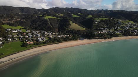 Picturesque-sandy-beach-surrounded-by-forested-hills-on-New-Zealand-shore,-Langs-Beach-aerial