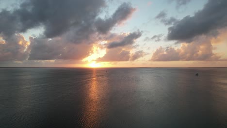 Perfekter-Blick-Auf-Das-Meer-Bei-Sonnenuntergang-Aus-Der-Luft,-Sonne-Am-Horizont-Und-Orangefarbene-Wolken-An-Einem-Strahlend-Blauen-Himmel