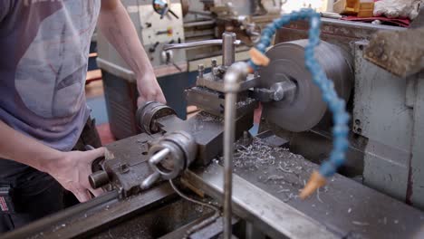 An-engineering-student-shaves-metal-from-a-large-metal-rod-on-a-metal-turning-lathe